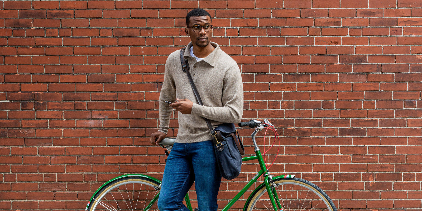Man standing next to a green bicycle against a brick wall